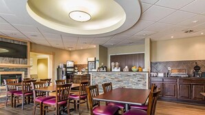 A restaurant with a central dining area featuring wooden tables and chairs, a stone accent wall, and a kitchen area with appliances and a coffee machine. - Quality Inn (Moncton)
