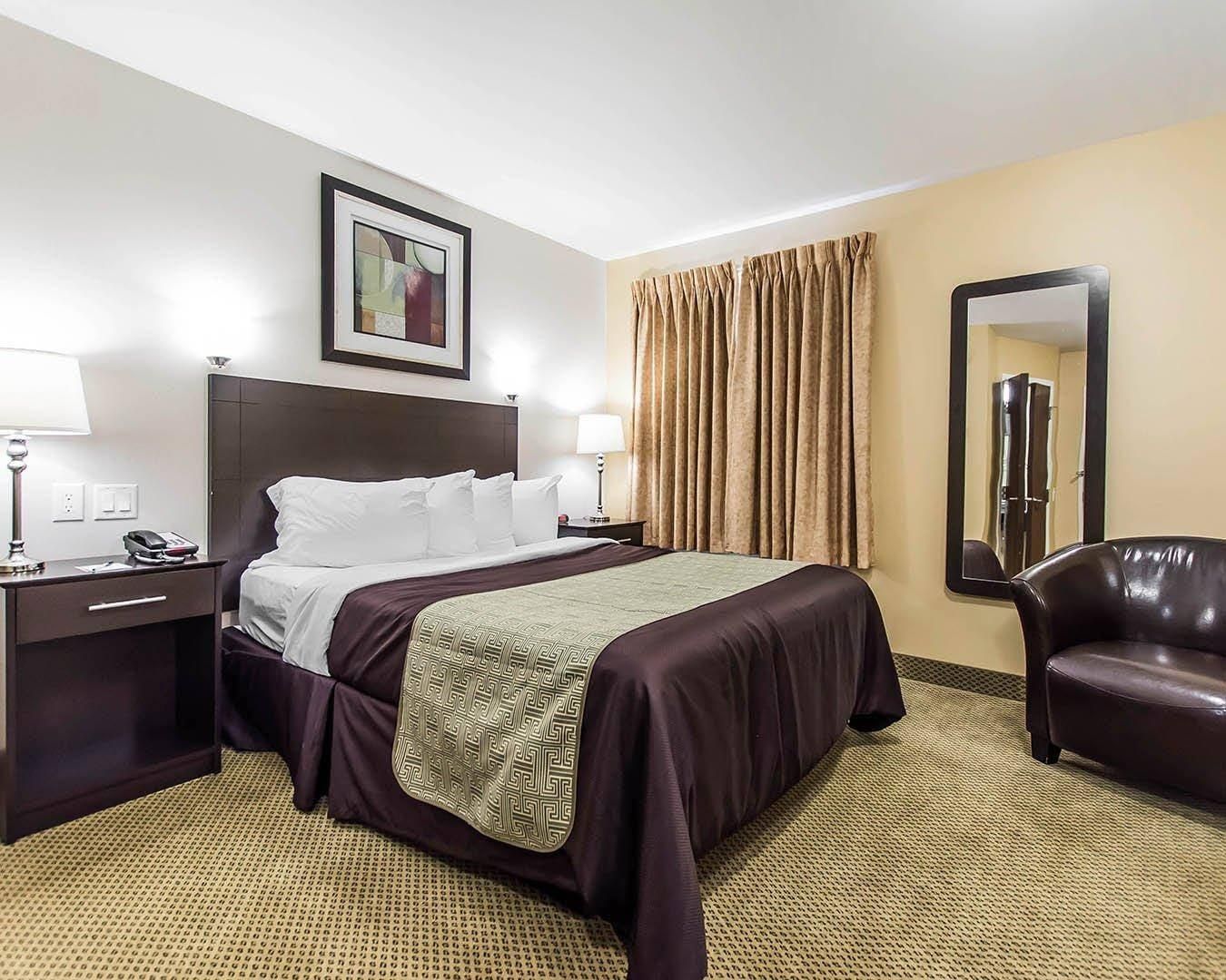 Une chambre d’hôtel avec un lit, des tables de chevet, une lampe, une chaise et un miroir.