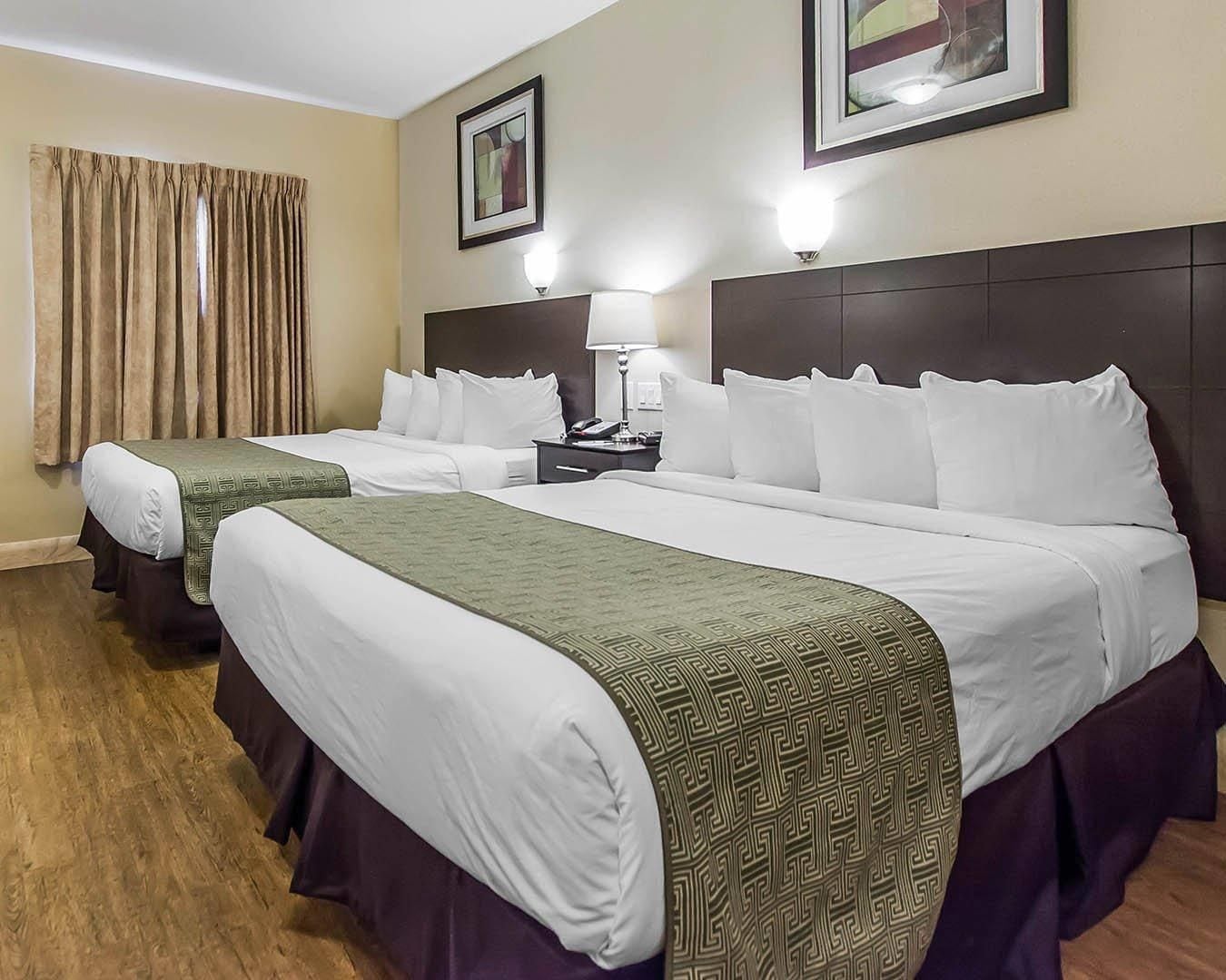 Een hotelkamer met twee bedden, een nachtkastje, een lamp en een ingelijst beeld aan de muur.