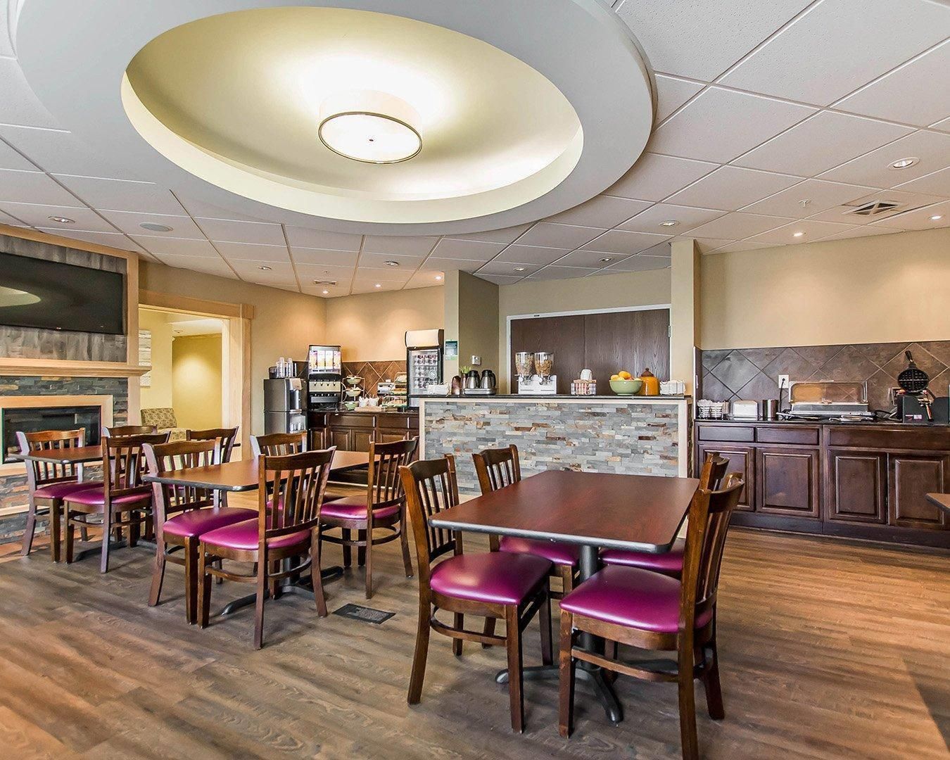 A restaurant with a central dining table surrounded by chairs, a kitchen area with appliances, and a stone accent wall.