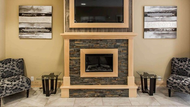 A fireplace with a stone surround and a TV above it, flanked by two chairs and two small tables. - Quality Inn (Moncton)