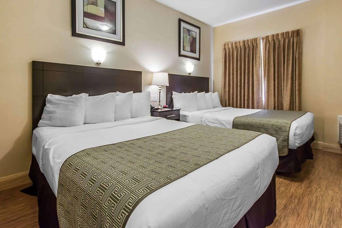 A hotel room with two beds, each with a patterned bedspread, a nightstand with a lamp, and framed artwork on the walls.
