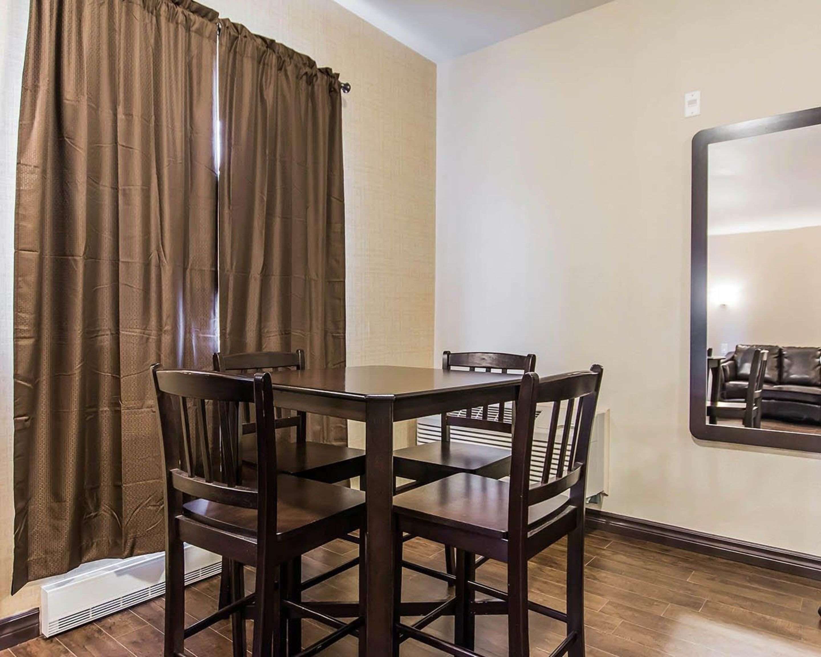 Un coin repas comprenant une table et quatre chaises, un rideau marron et un miroir fixé au mur.