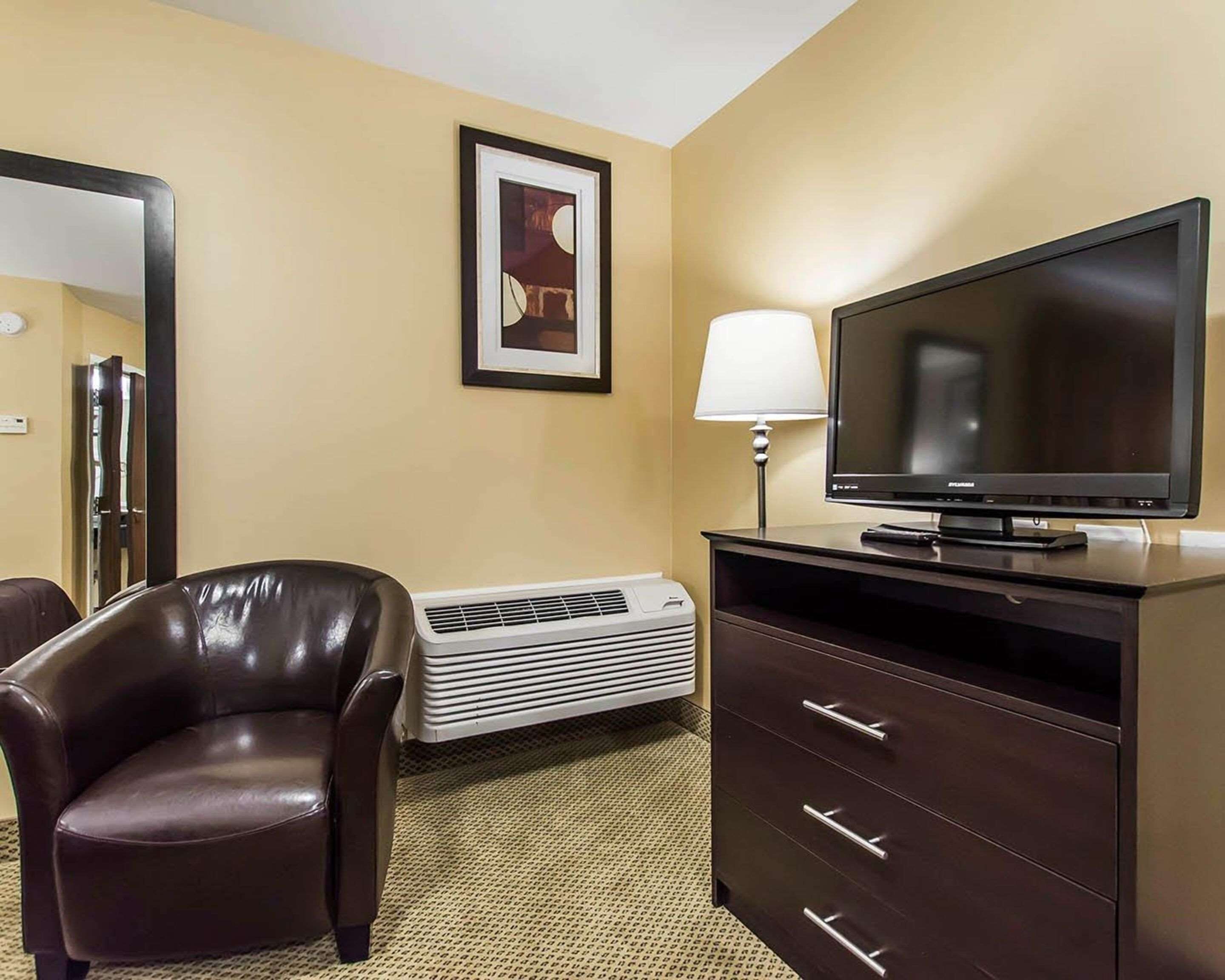 A hotel room with a leather chair, a flat-screen TV, a desk with drawers, a lamp, and a framed picture on the wall.