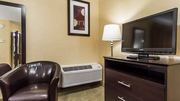 A hotel room with a leather chair, a flat-screen TV, a desk with drawers, a lamp, and a framed picture on the wall.
