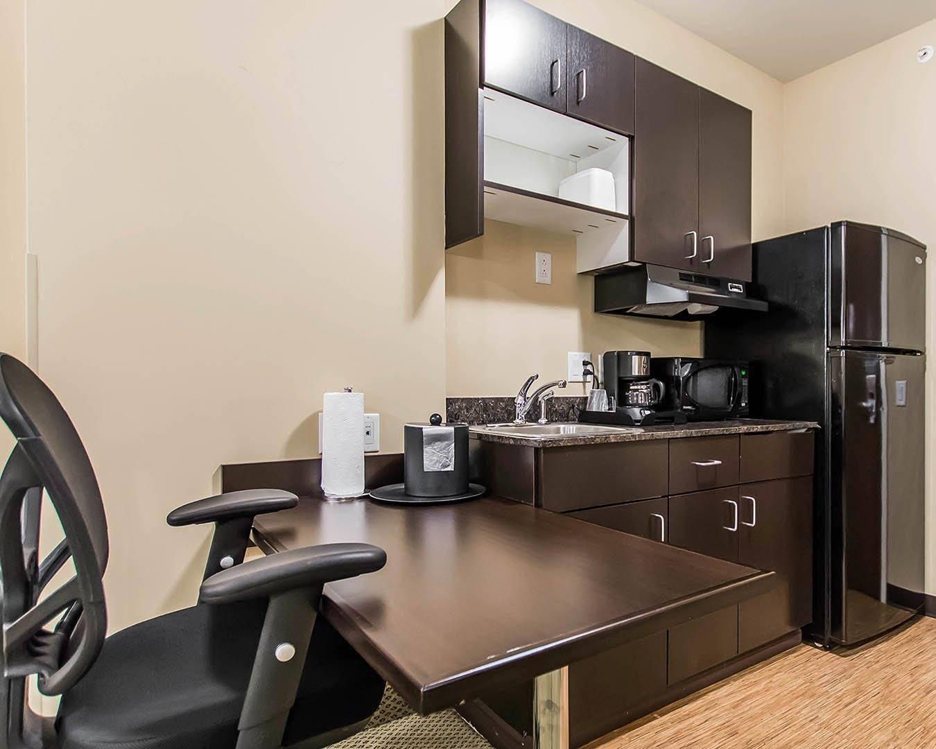 A compact kitchenette with a dark countertop, a black refrigerator, a coffee maker, and a microwave.