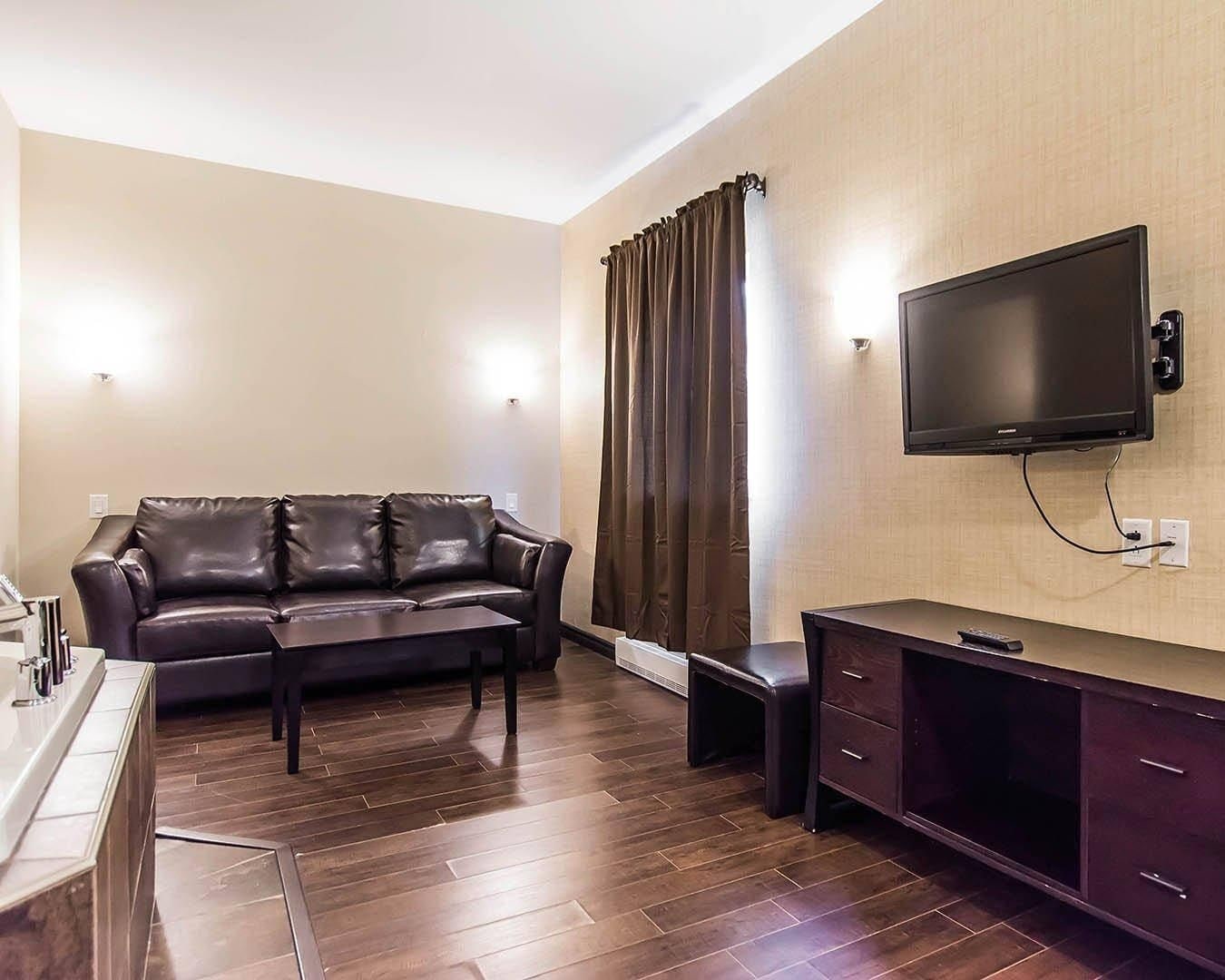 Ein Wohnzimmer mit einer Ledersofa, einem Couchtisch, einem an der Wand montierten Fernseher und einem Holzboden.