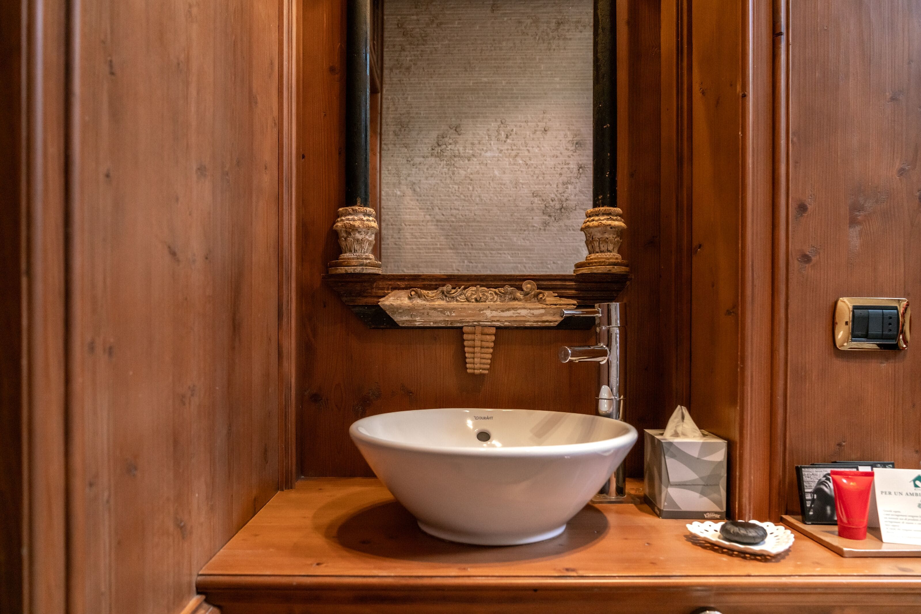 A wooden bathroom with a white sink, a mirror, and a towel dispenser.