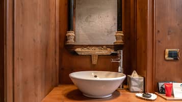 A wooden bathroom with a white sink, a mirror, and a towel dispenser.