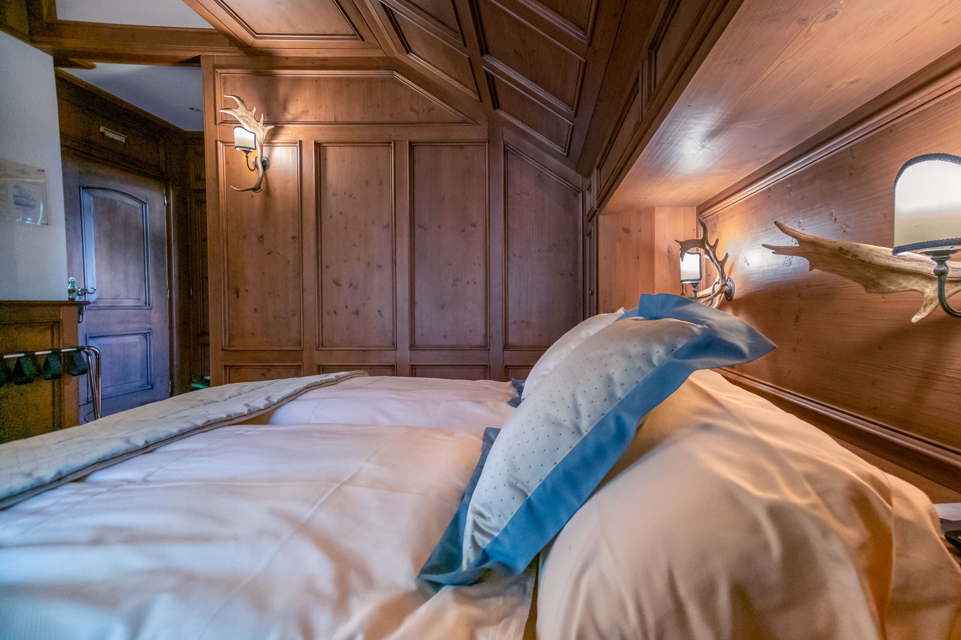 A wooden room with a bed, a door, and wall-mounted lights.