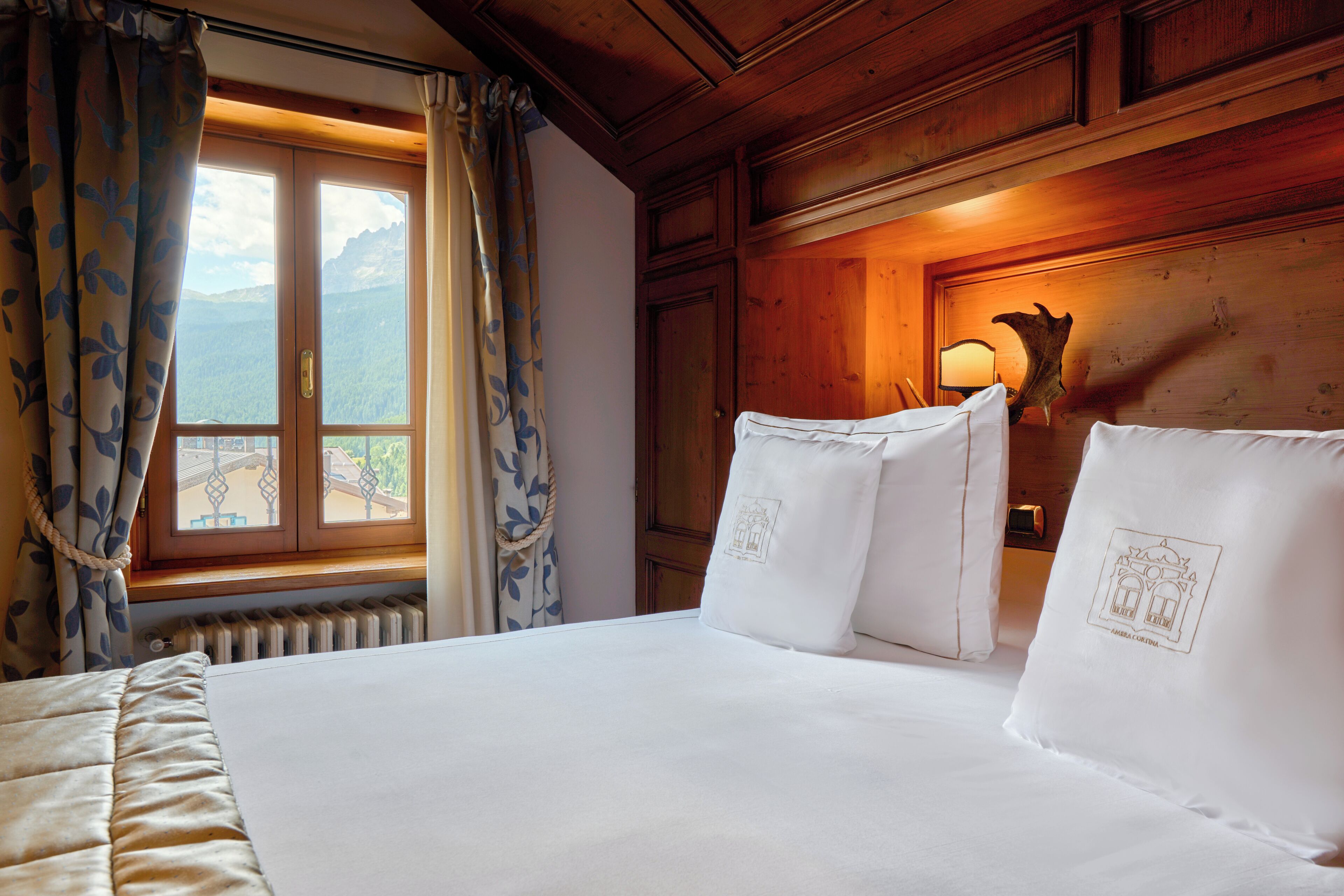 Habitación de hotel con una cama grande, una ventana con cortinas, un cabecero de madera y una lámpara de pared.