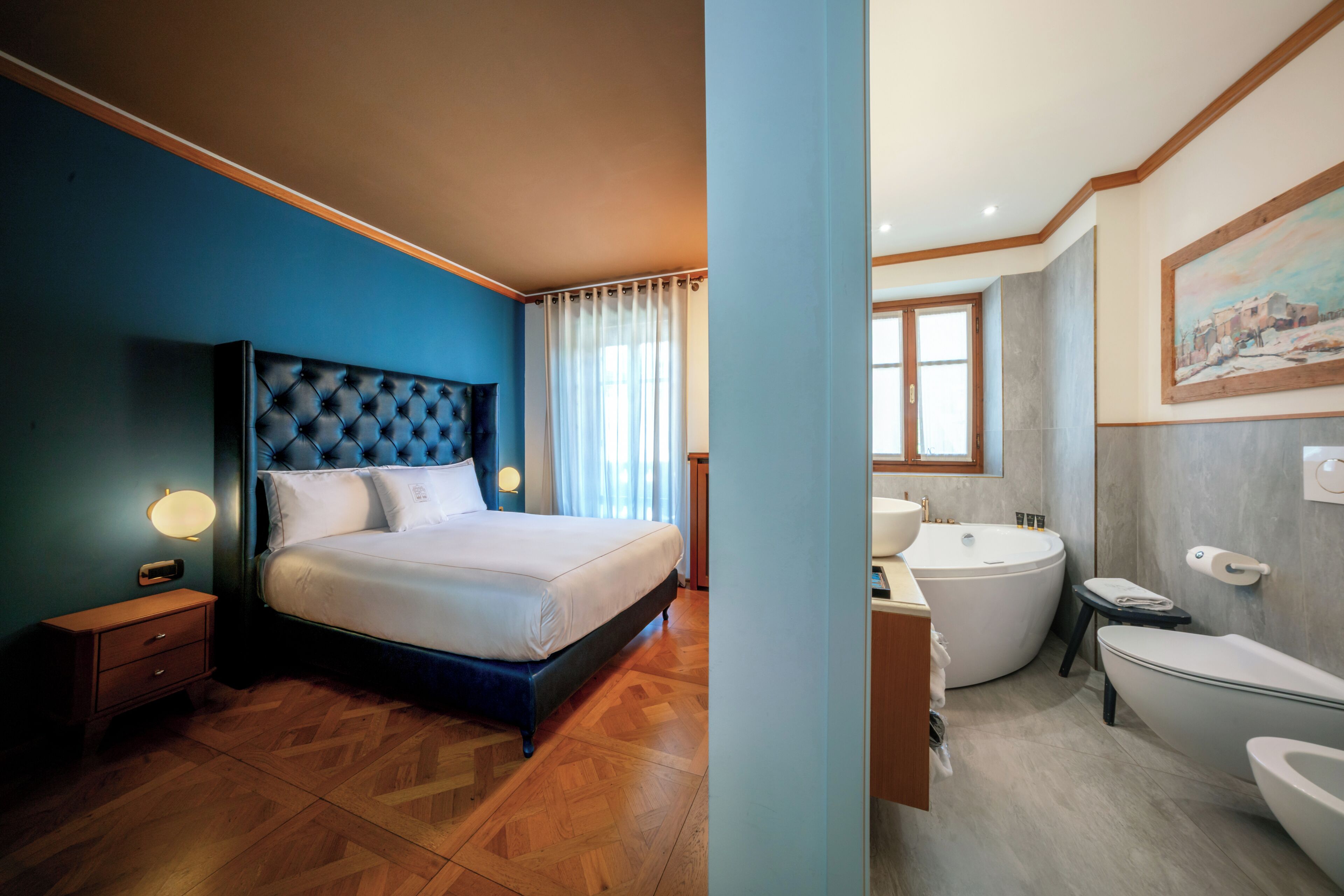 A bedroom with a large bed, a nightstand, and a bathroom with a bathtub, toilet, and sink.