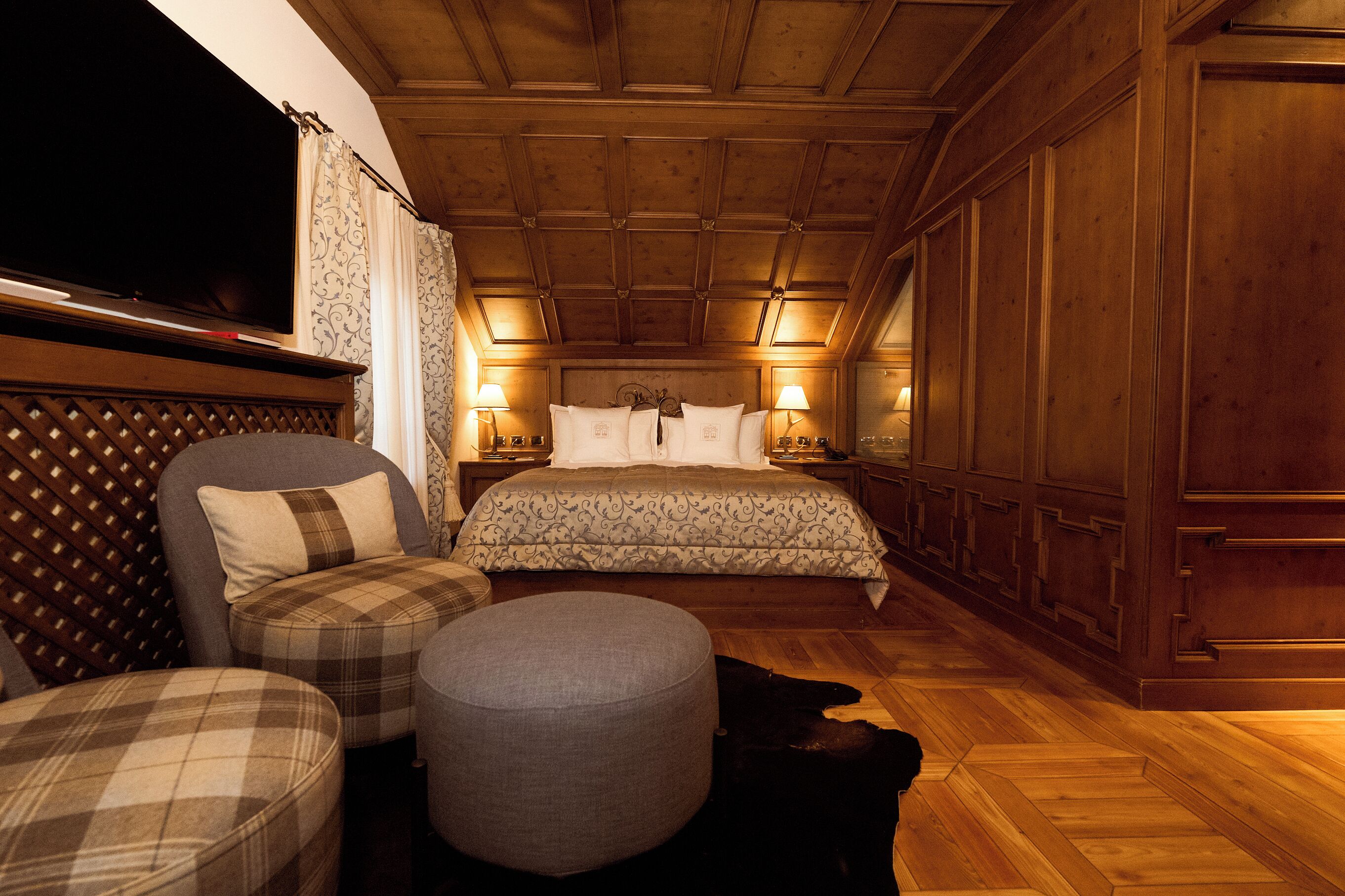 Une chambre à coucher comprenant un lit, deux tables de chevet, une télévision, un canapé, un pouf et une armoire en bois.