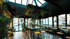 A restaurant with high ceilings, hanging plants, and a view of the street.