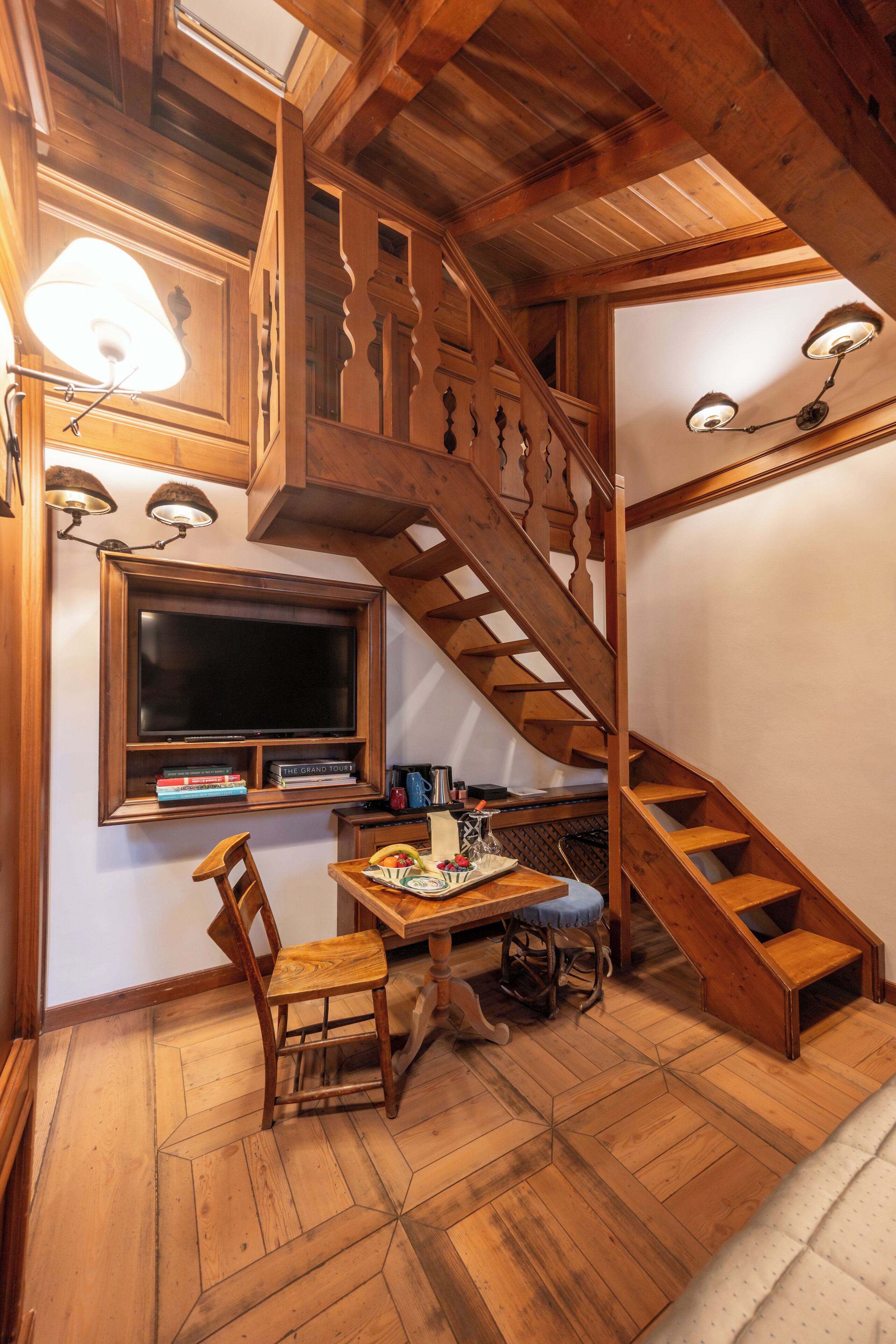 A wooden staircase with a built-in desk and chair, a window above, and a television on the wall.