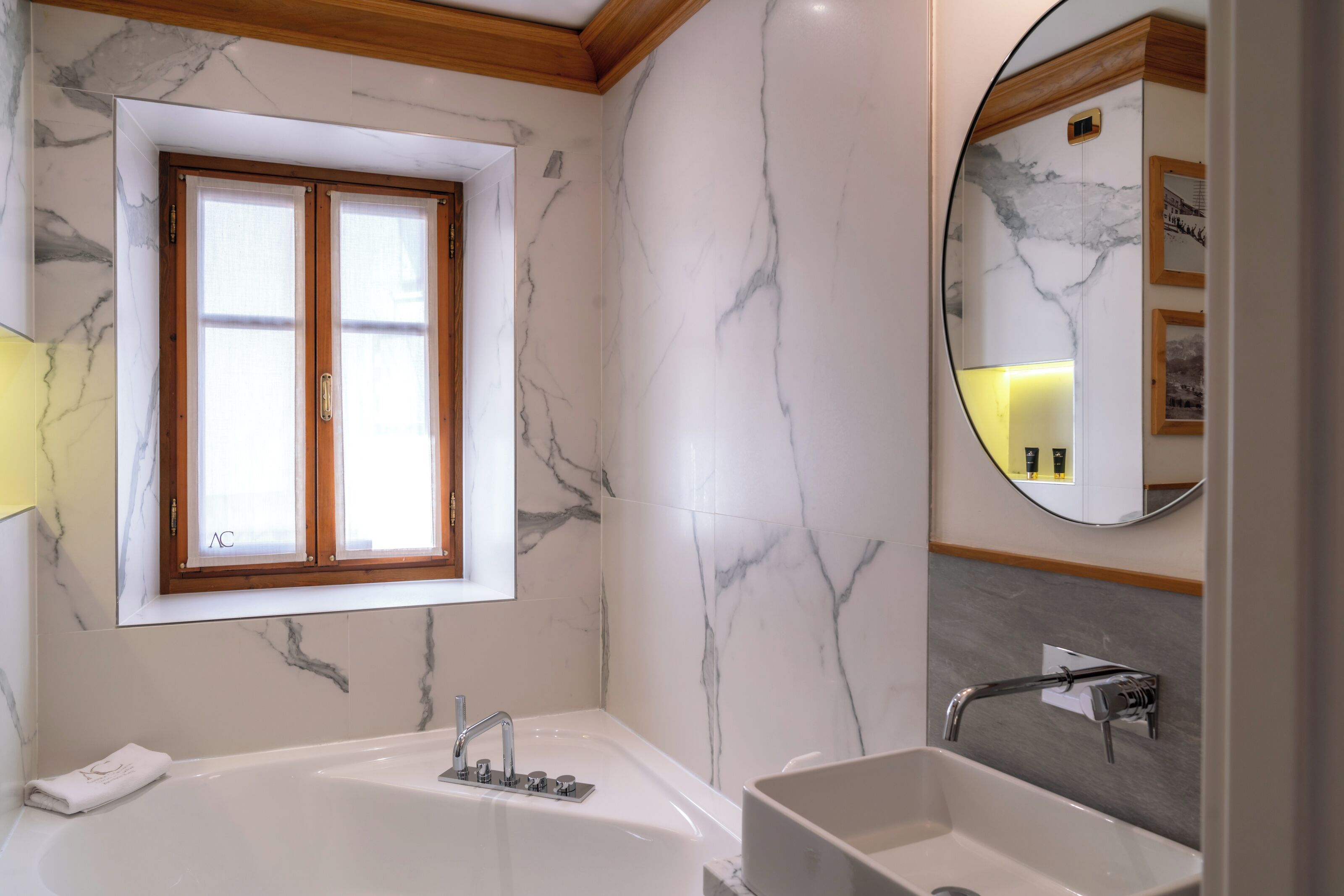 Un baño moderno con pared de mármol, una bañera grande, un lavabo y una ventana con marcos de madera.