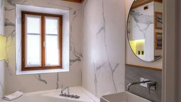 Un baño moderno con pared de mármol, una bañera grande, un lavabo y una ventana con marcos de madera.