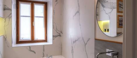 A modern bathroom with a marble wall, a large bathtub, a sink, and a window with wooden frames.