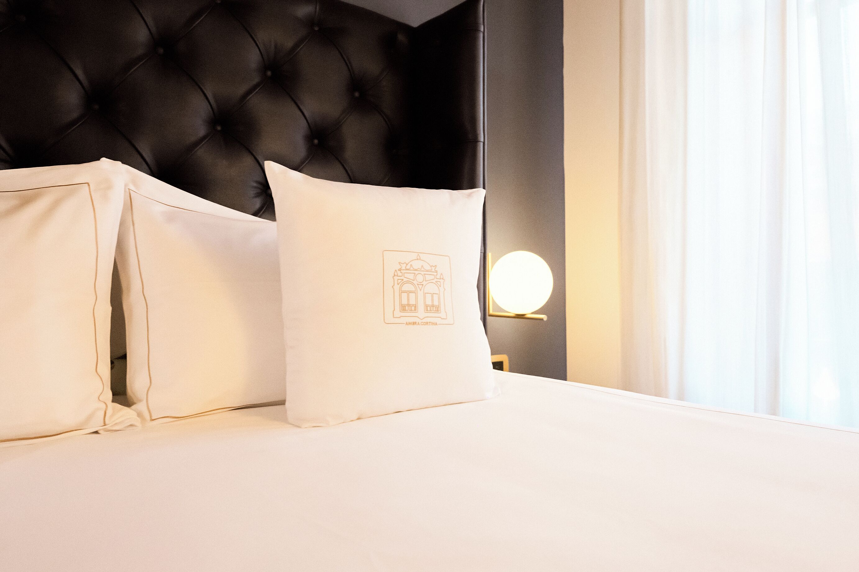 Una cama bien hecha con dos almohadas, un cabecero capitonado y una lámpara de noche.