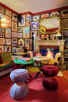 Una habitación con chimenea, un sofá, dos otomanas, una mesa de centro y una pared decorada con obras de arte enmarcadas.