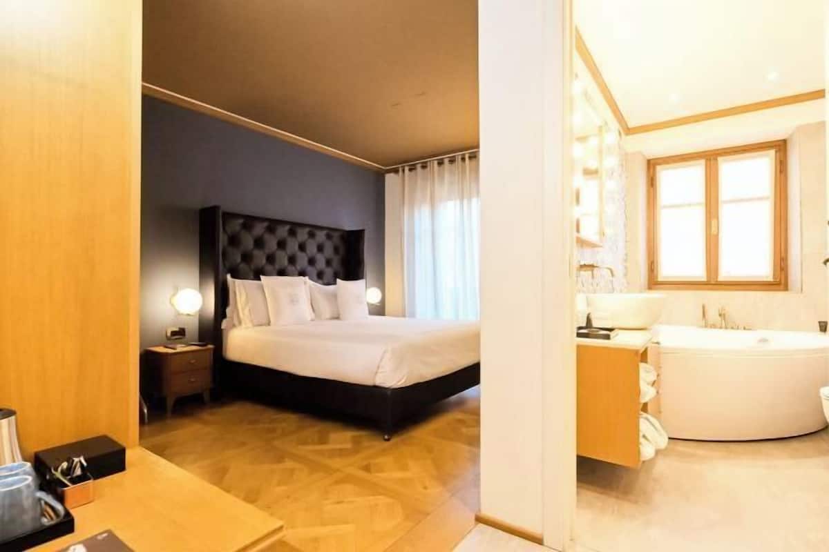Une chambre d’hôtel comprenant un lit, une table de chevet, une lampe et une salle de bain avec une baignoire et un lavabo.