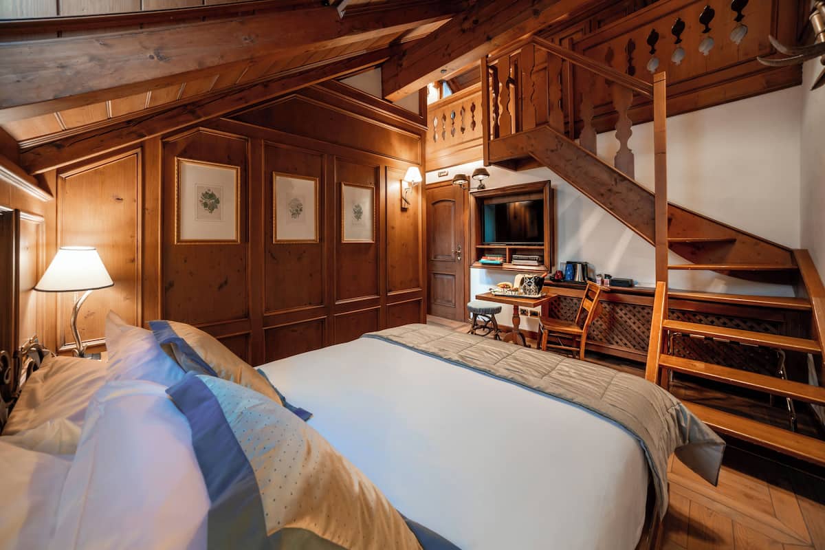 Une chambre confortable avec un grand lit, des murs en bois, un bureau et un escalier.