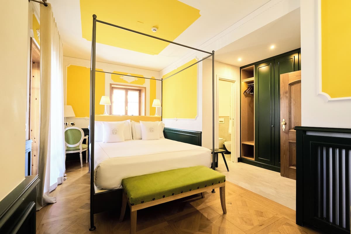 Un lit à baldaquin avec un banc vert, un plancher en bois, une armoire verte et une chaise blanche.