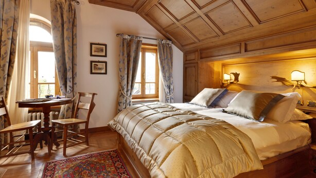 A bedroom with a large bed, wooden ceiling, and a table with chairs.