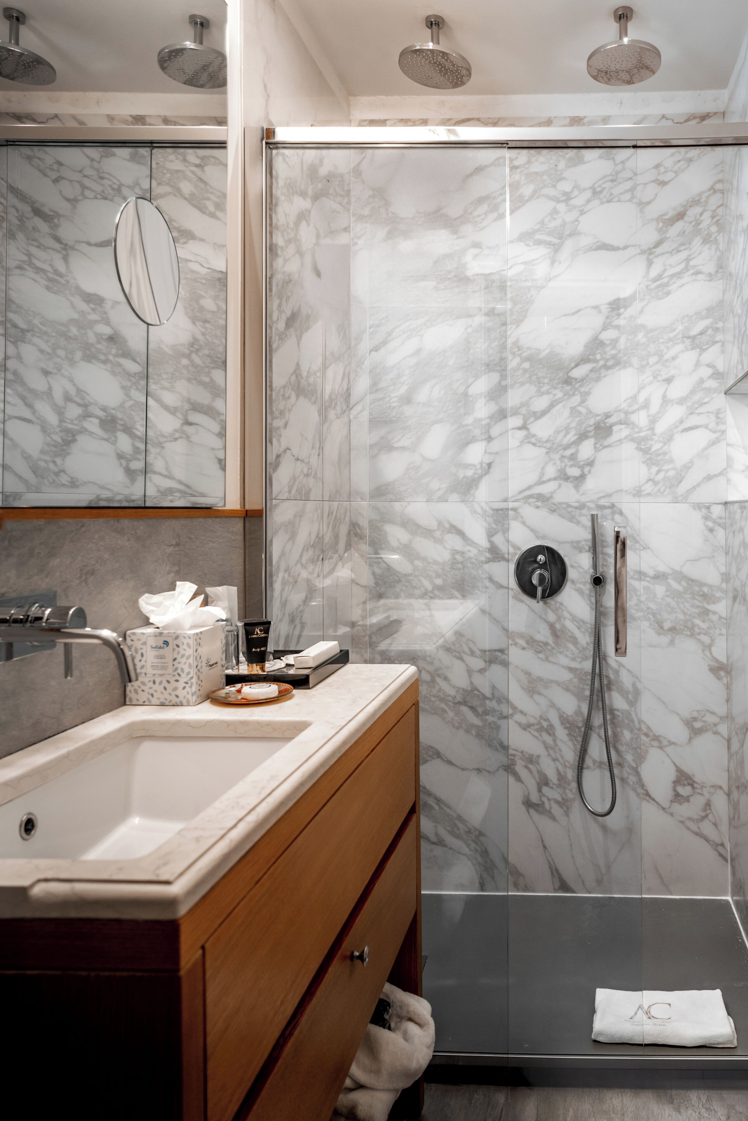 Un baño con pared de mármol, un lavabo, un espejo y una ducha con cabezal de ducha de mano.