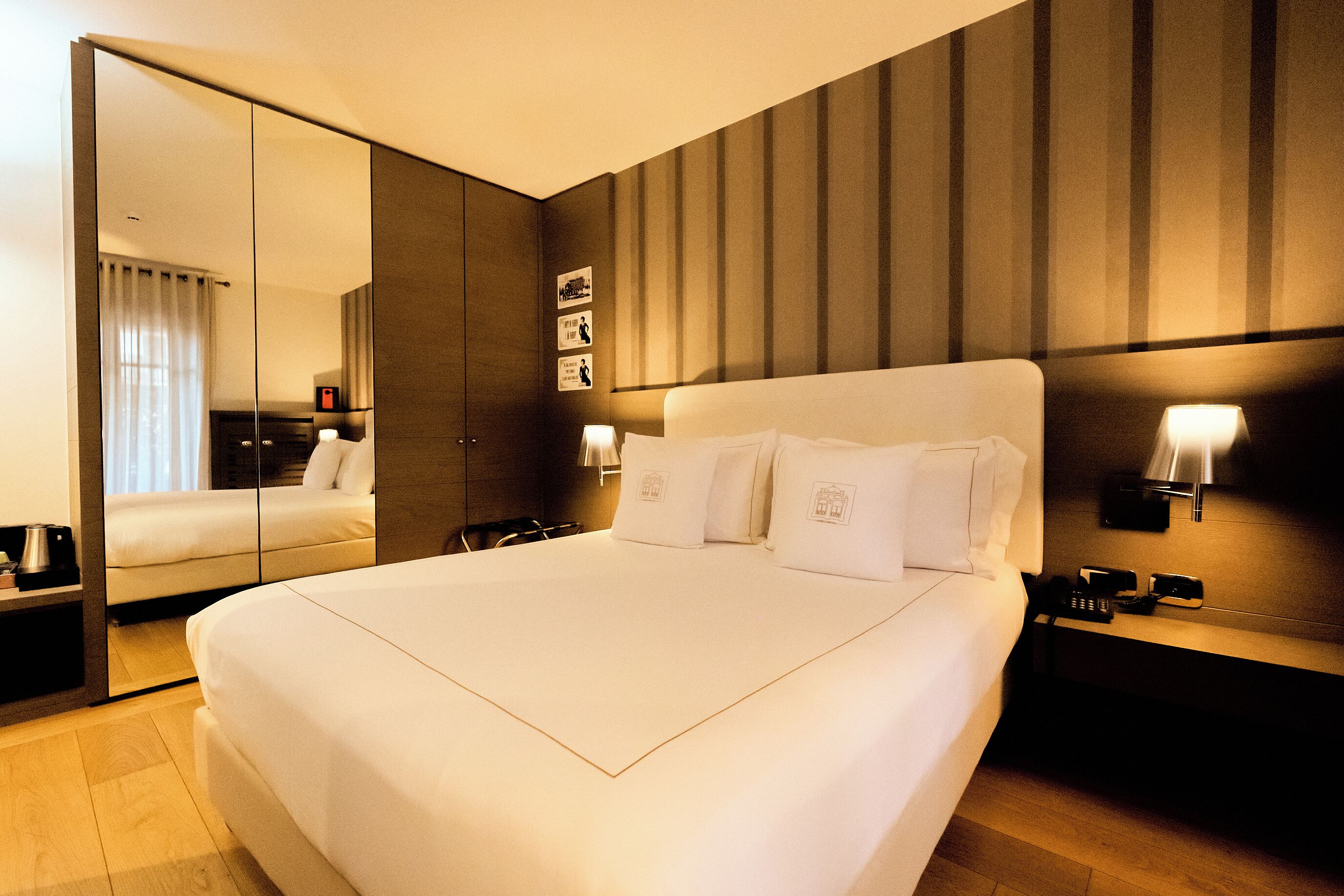 Een hotelkamer met een groot bed, een spiegel, een nachtkastje en een wandlamp.