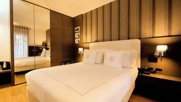 Una habitación de hotel con una cama grande, un espejo, una mesita de noche y una lámpara de pared.