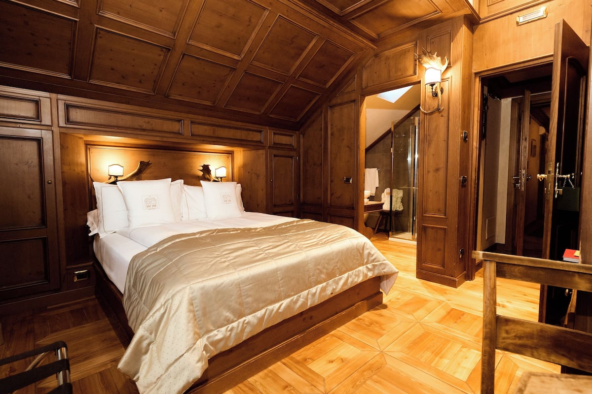 Une chambre aux murs lambrés, avec un grand lit, une table de chevet et un luminaire fixé au mur.