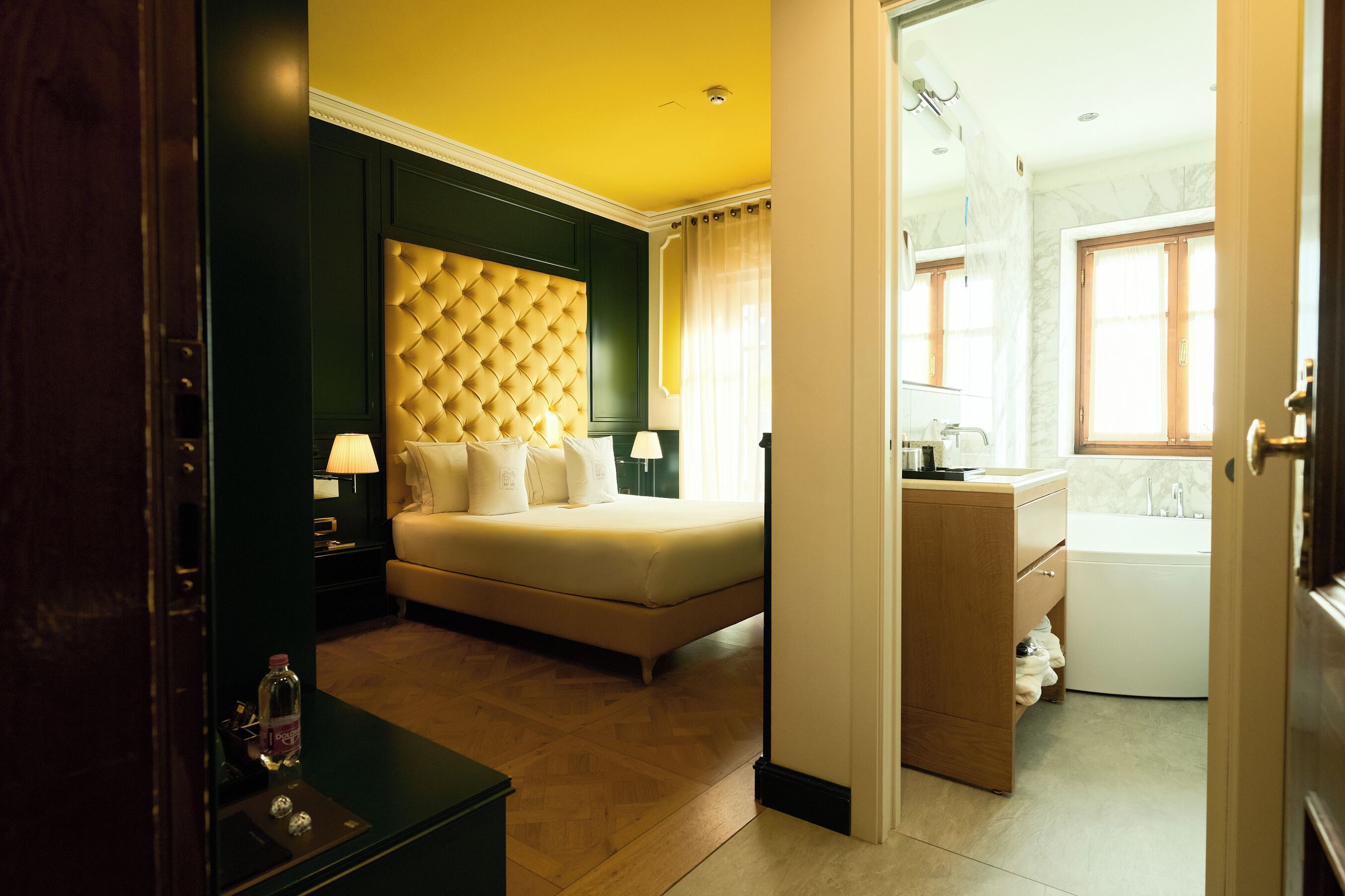A hotel room with a bed, bedside tables, a wardrobe, and a bathroom visible through an open door.
