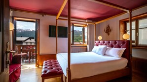 A four-poster bed with a view of mountains, a red upholstered bench, and a wooden floor.