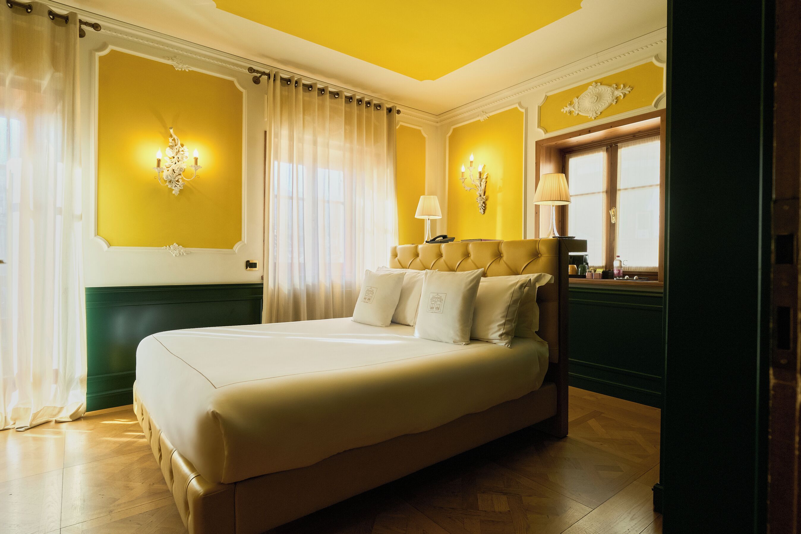 Uma cama grande com lençóis brancos, uma parede verde de destaque e um candelabro.