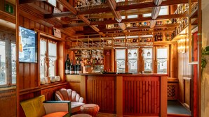 A cozy bar area with wooden paneling, a seating area with colorful cushions, and a variety of bottles and glasses on shelves.