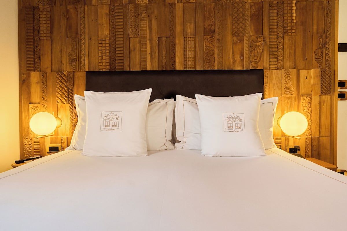 Une chambre d’hôtel avec une tête de lit en bois, un lit recouvert de draps blancs et deux lampes de chevet.