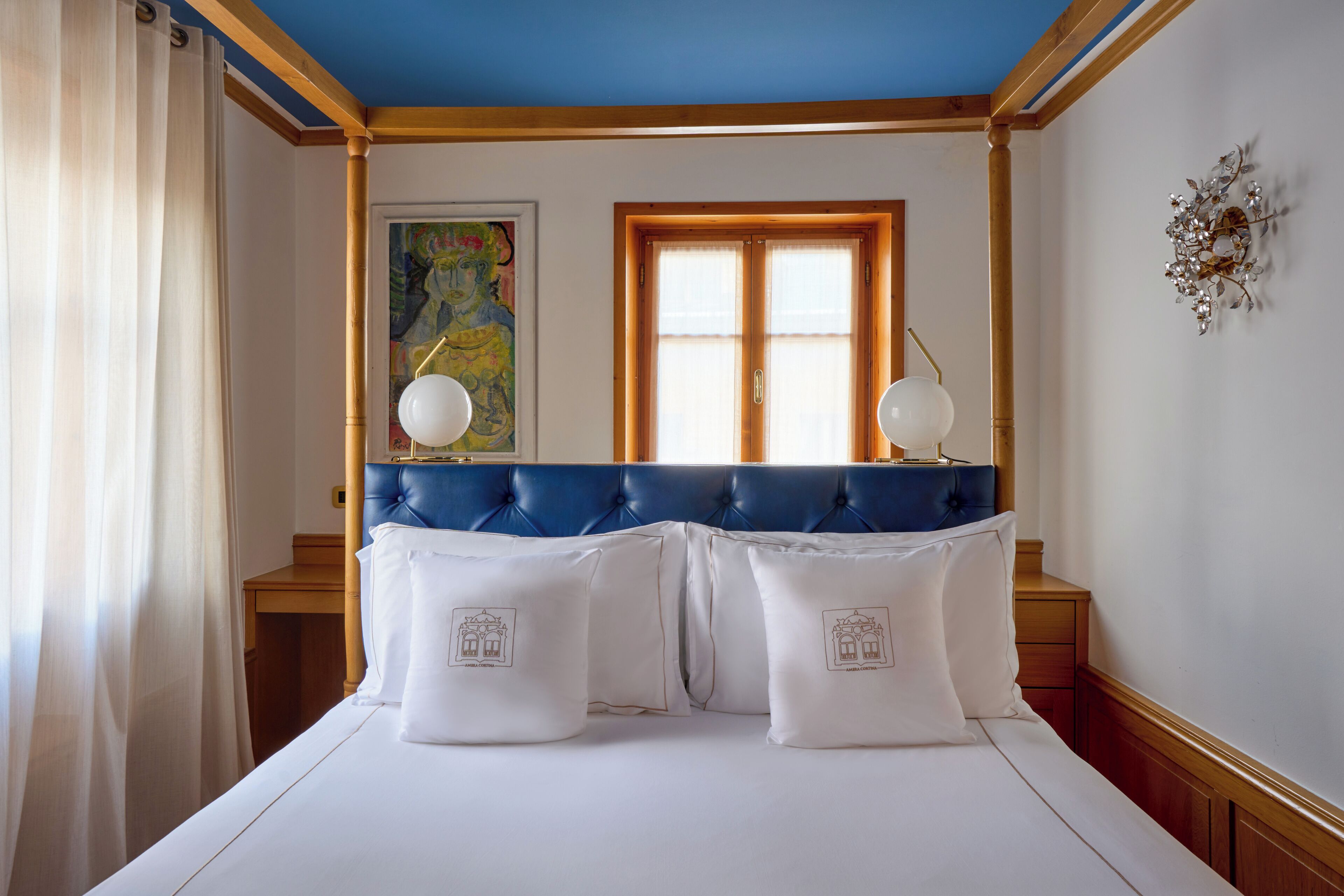 A hotel room with a blue headboard, white bedding, and a window with curtains.