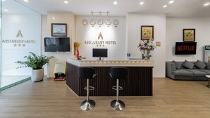 A reception area with a wooden reception desk, two black bar stools, a flat-screen TV, a clock, and a sign for A25 Luxury Hotel. - A25 Premium Hotel - 29 Bui Thi Xuan (Ho Chi Minh City)