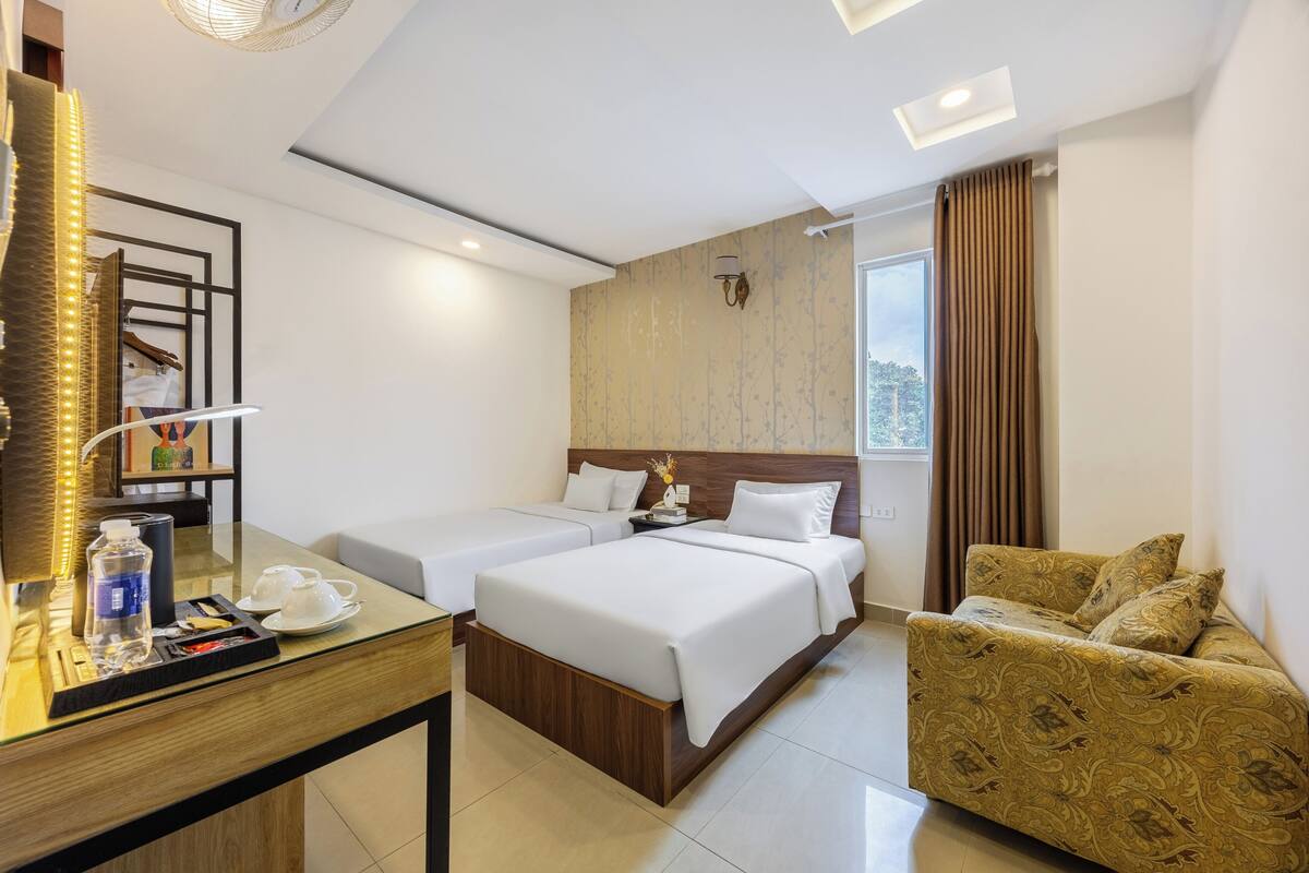 Une chambre d’hôtel comprenant un lit, deux tables de chevet, un canapé, un bureau avec un miroir et une fenêtre avec des rideaux.
