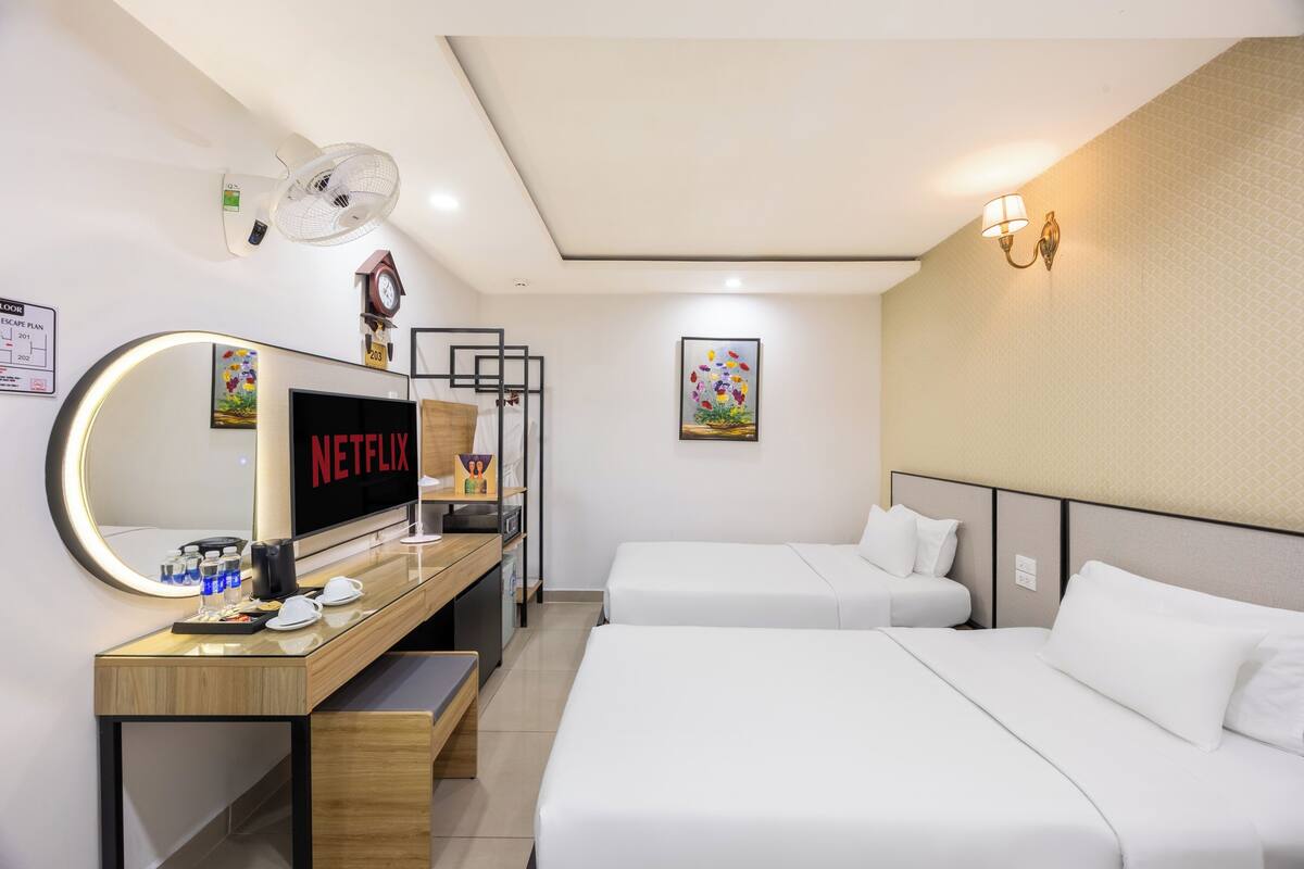 Une chambre d’hôtel comprenant un lit, un bureau avec un téléviseur affichant « NETFLIX », une table de chevet, un miroir, une horloge murale et un luminaire fixé au mur.