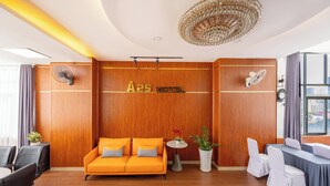 A hotel reception area with a wooden wall, a sofa, a small table with a plant, and a fan. - A25 Premium Hotel - 29 Bui Thi Xuan (Ho Chi Minh City)