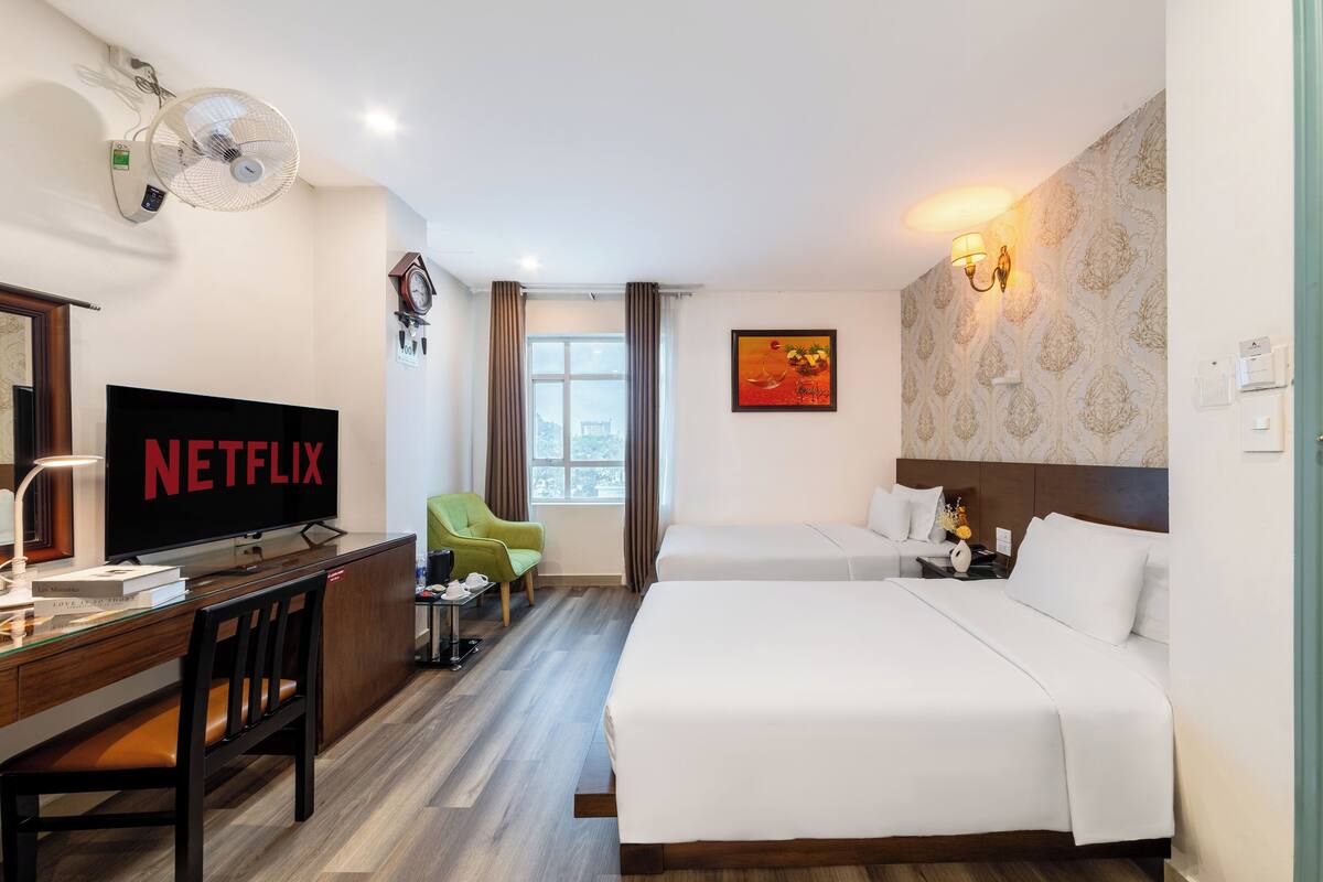 Une chambre d’hôtel comprenant un lit, un bureau avec une télévision, une chaise, une table de chevet et une fenêtre avec des rideaux.