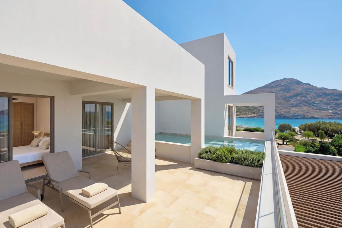 Habitació d'hotel moderna amb balcó, un llit, zona de seients i vista al mar.