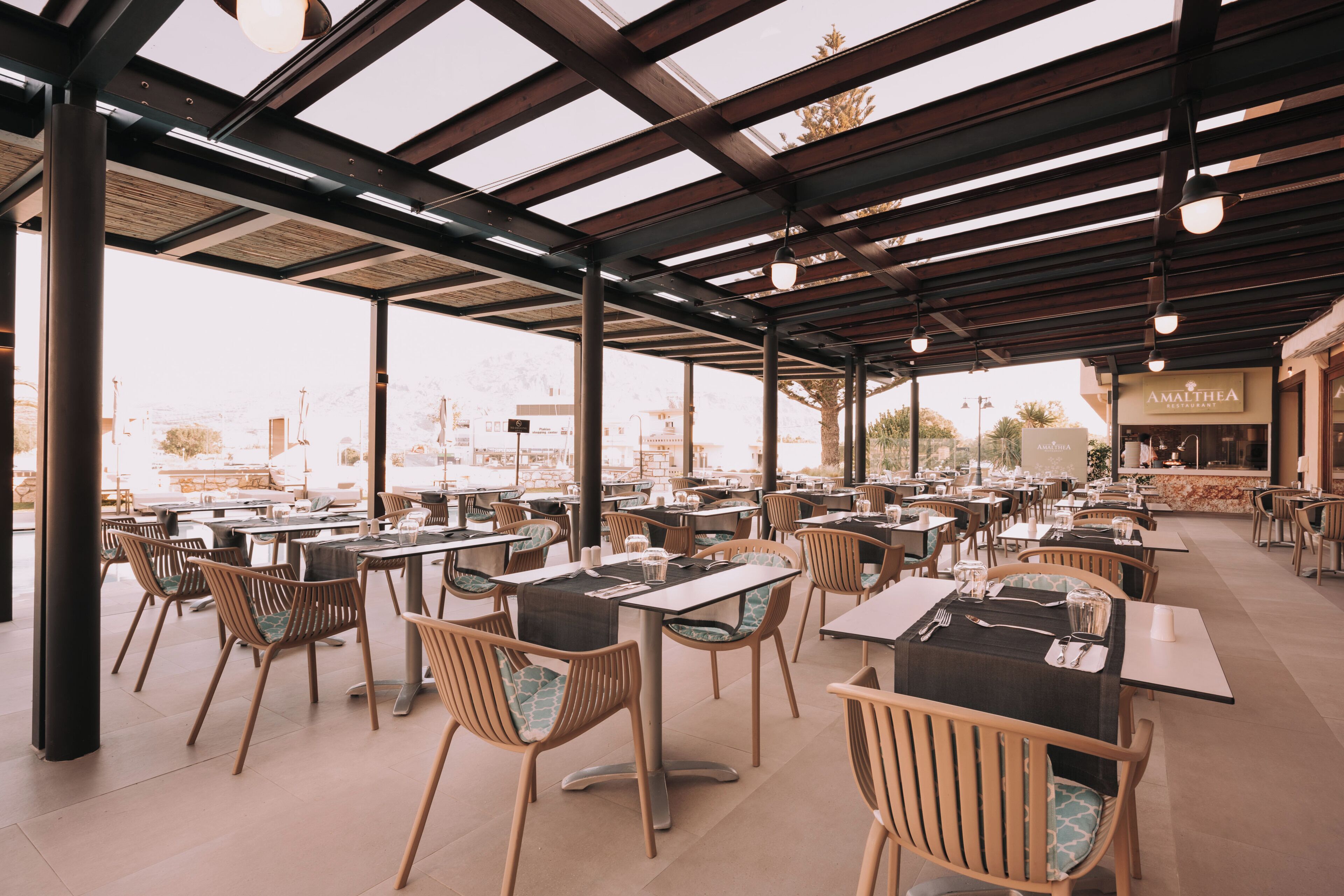 Un área de comedor al aire libre con mesas y sillas, una sección cubierta con vistas, y un letrero de restaurante.
