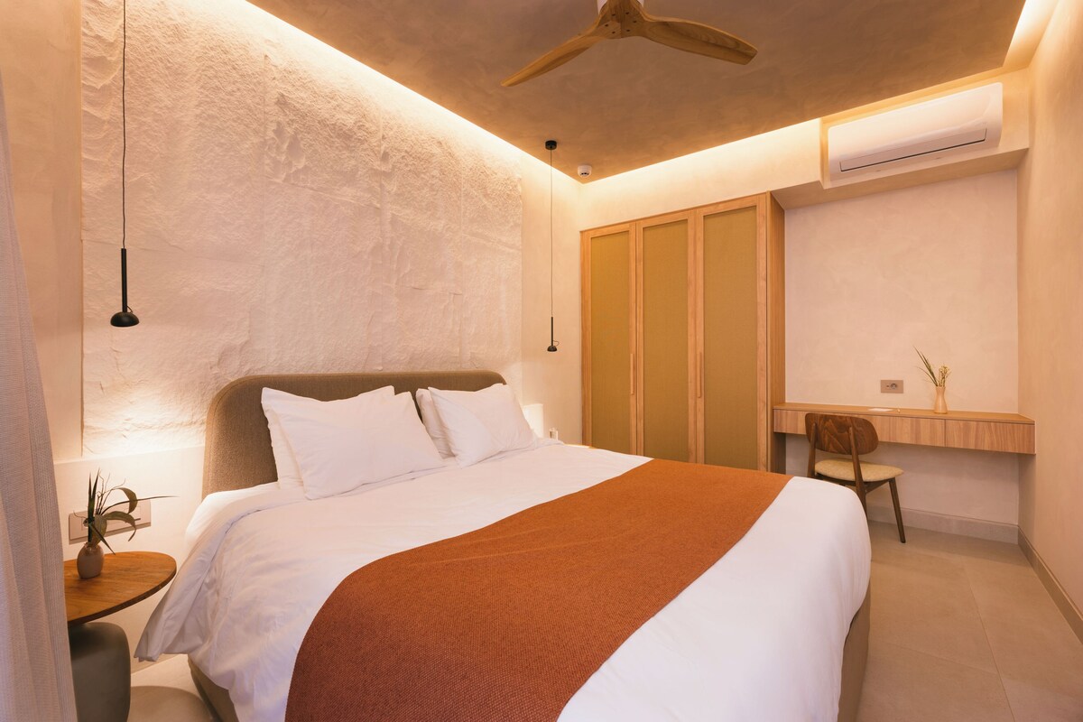 A modern bedroom with a bed, bedside table, and a desk with a chair.