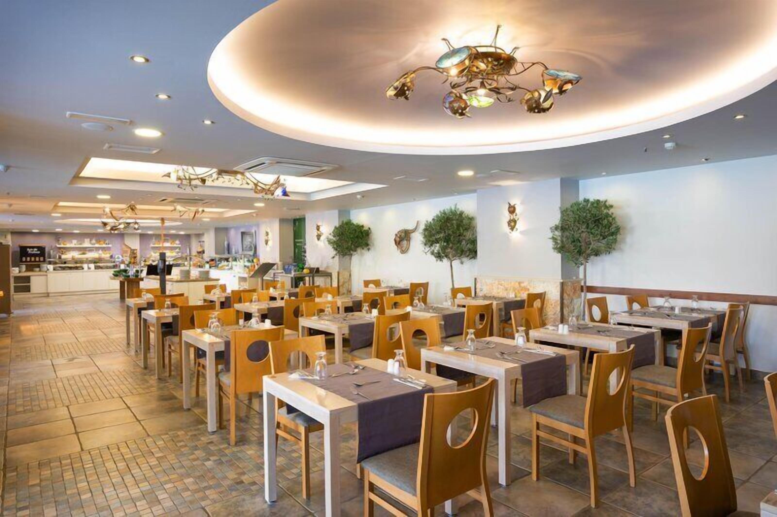 En rymlig restaurang med flera matbord och stolar, en modern takdesign och en stilren, väl upplyst interiör.