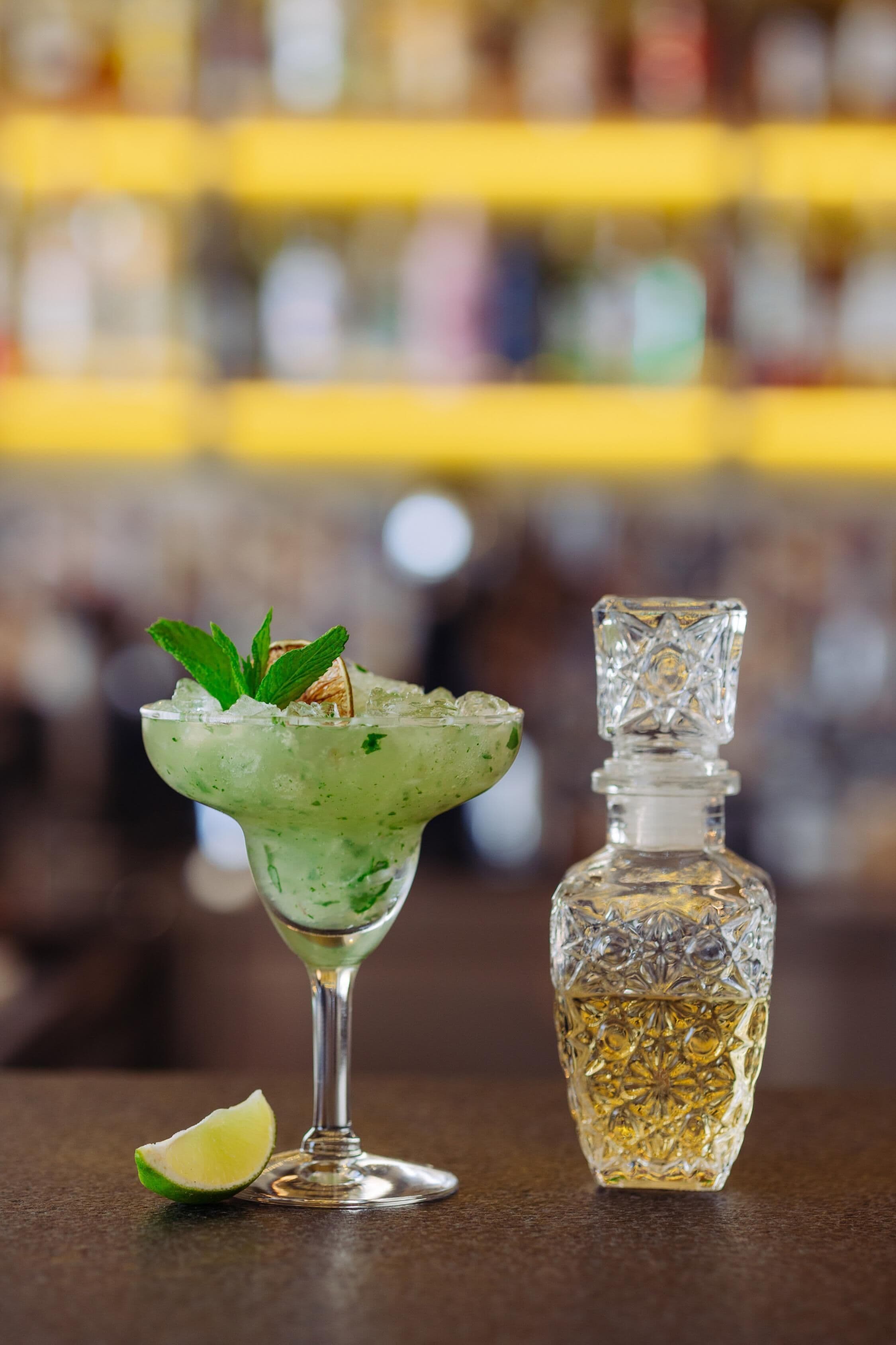A cocktail glass with a lime wedge and mint garnish on a bar counter.