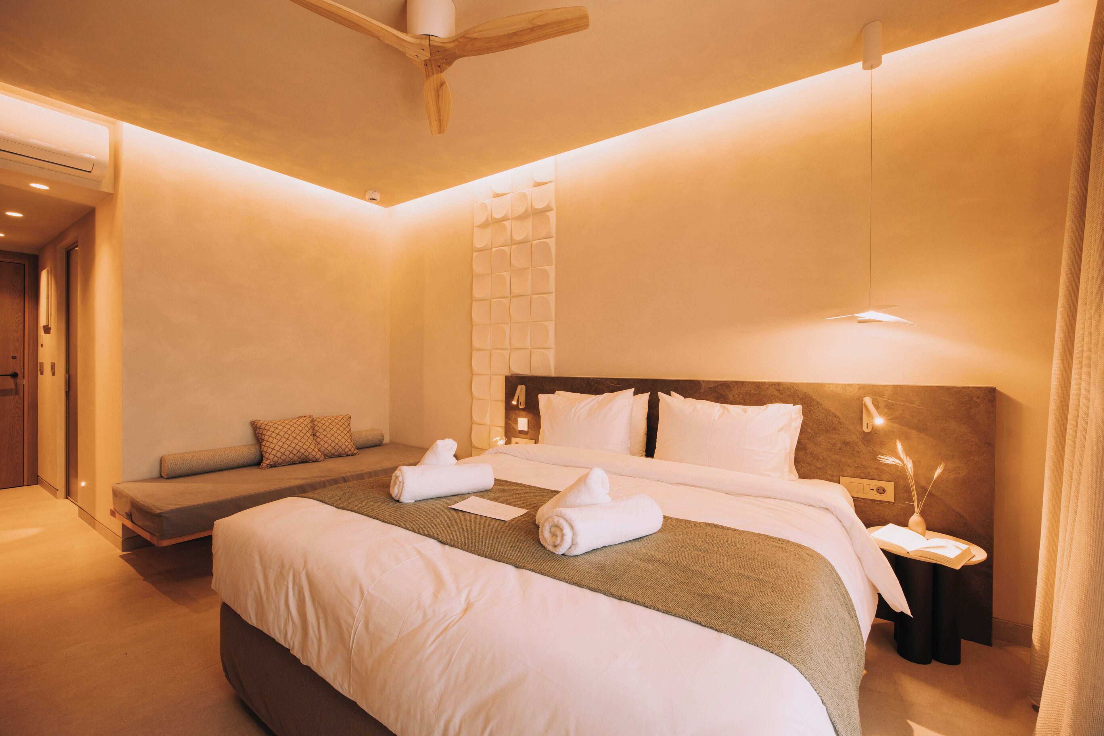 Habitació d'hotel amb un llit, una taula de nit, una làmpada de paret i un ventilador de sostre.