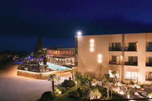 A hotel with a swimming pool, outdoor seating, and a well-lit facade.